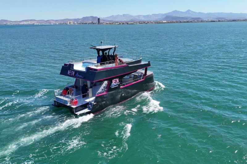 Neon Moon party catamaran with a black hull cruising off Cabo San Lucas