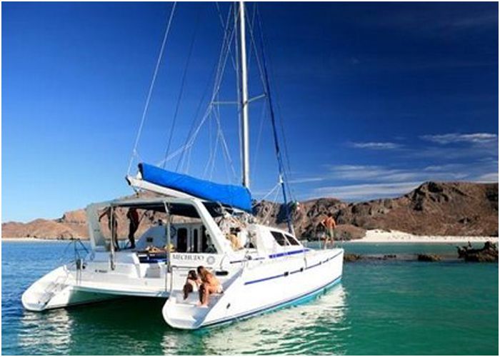 Sailing catamaran anchored off a sandy beach beneath desert mountains