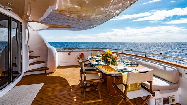 Aft deck of a yacht set with a dining table, flowers and an ocean view