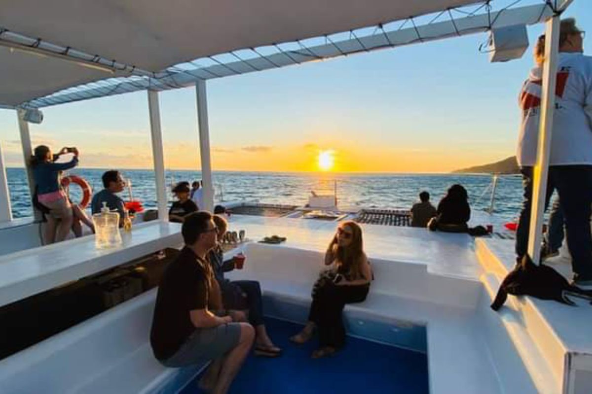 Guests on a catamaran deck watching the sunset over the Pacific