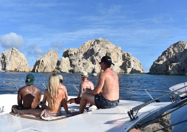 Friends relaxing on the bow of a yacht in front of the rock formations of Land's End