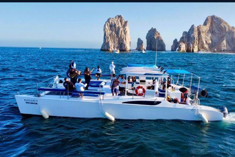 Party catamaran with guests on deck near the rock pinnacles of El Arco