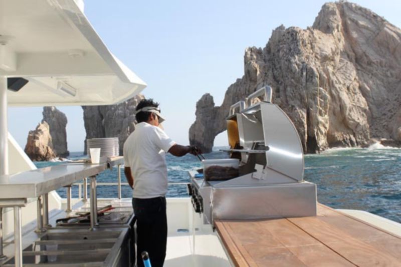 Onboard chef grilling on deck with the rocks of Land's End behind