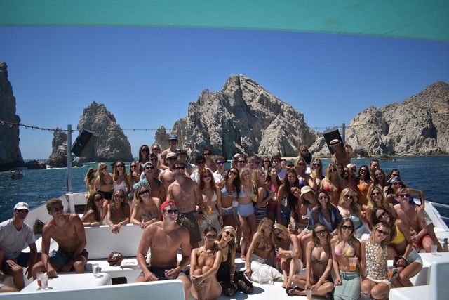 Large group of guests posing on the bow of a boat in front of the rocks at Land's End