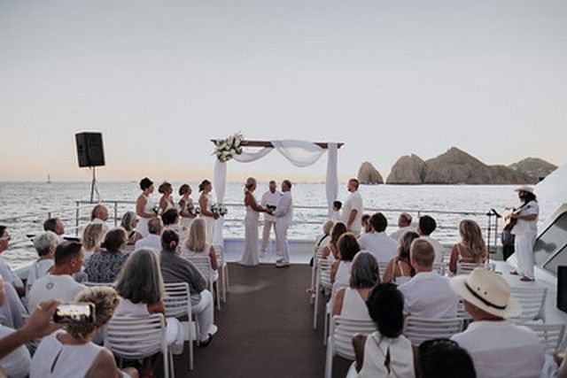 Guests dressed in white seated for a wedding ceremony on a catamaran facing Land's End