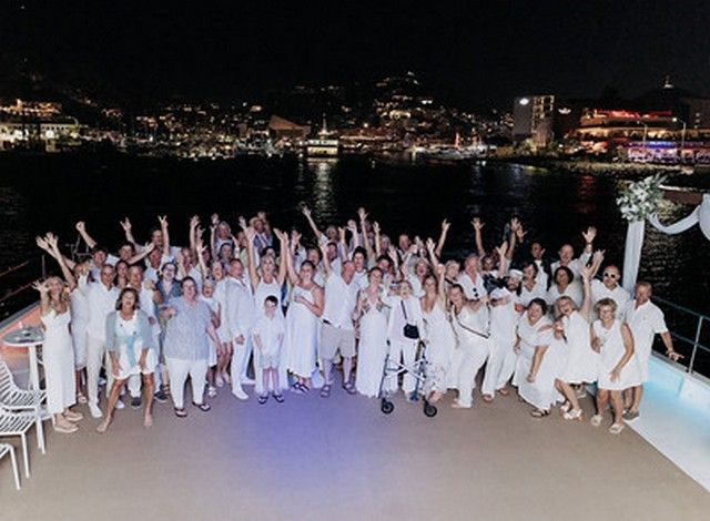 Wedding guests dressed in white celebrating on deck at night with the lights of Cabo behind